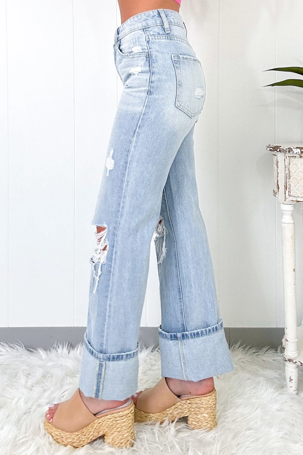 Side view of light wash distressed high-rise wide leg jeans showing cuffed hem and zipper detail